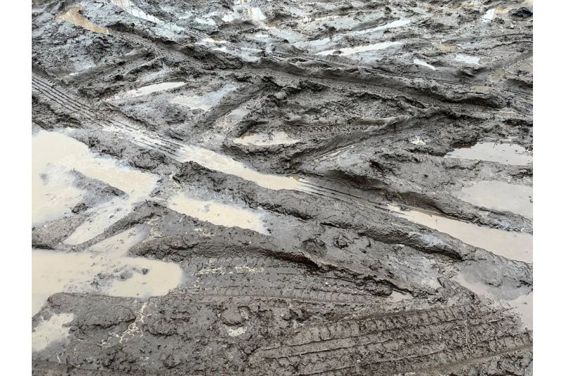 Muddy terrain filled with tyre tracks and puddles after heavy rain in an outdoor construction site.